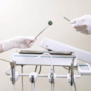 Two people's hands holding exam tools by tray of dental equipment